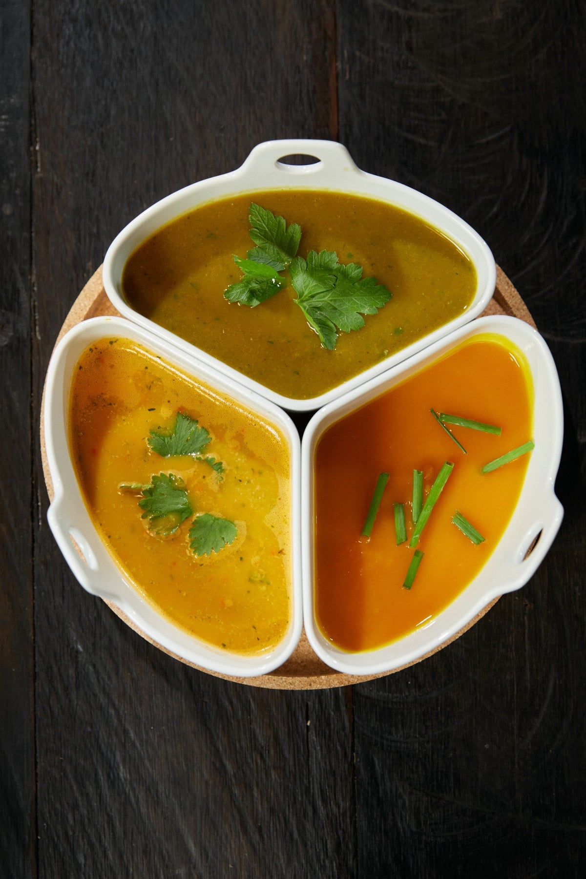 Trois soupes servies dans un plat à compartiments, herbes fraîches